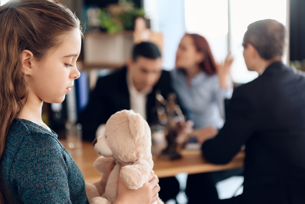 Child Holding A Toy Bear While Parents are arguing